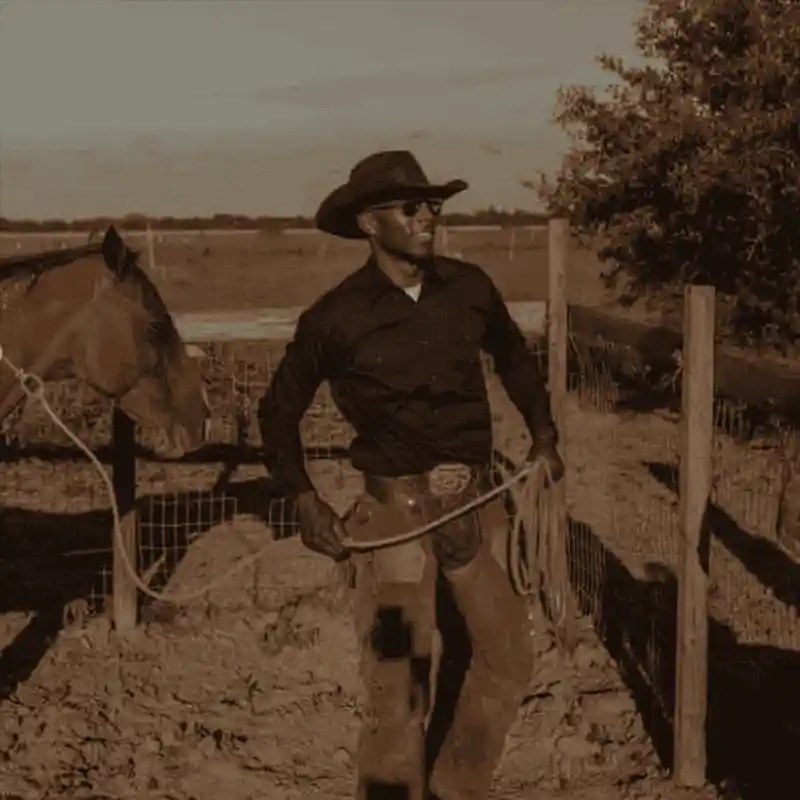 Cowboy wearing a hat and a belt buckle with a horse on a plain